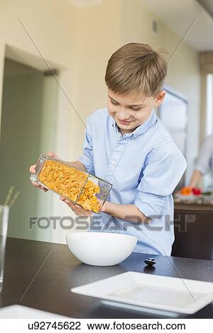 Smiling boy pouring corn flakes in bowl at home View Large Photo Image Stock Image - Smiling boy pouring corn flakes in bowl at home. Fotosearch