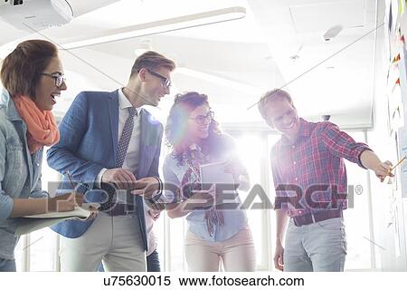 Stock Photography - Smiling businessman explaining to colleagues in creative office. Fotosearch