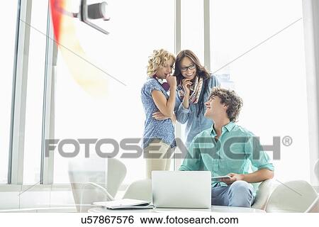Smiling businessman looking at female colleagues gossiping in creative office View Large Photo Image Stock Photograph - Smiling businessman looking at female colleagues gossiping in creative office. Fotosearch