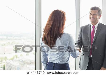 Stock Photo - Smiling businessman shaking hands with businesswoman in office. Fotosearch
