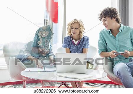 Smiling businesspeople discussing at table in creative office View Large Photo Image Stock Photograph - Smiling businesspeople discussing at table in creative office. Fotosearch