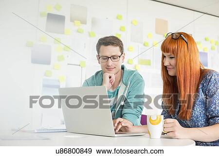 Smiling businesspeople using laptop at desk in creative office View Large Photo Image Stock Photo - Smiling businesspeople using laptop at desk in creative office. Fotosearch