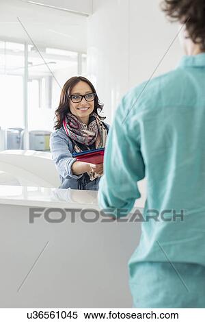 Smiling businesswoman handing over to male colleague at counter in creative office View Large Photo Image Stock Photography - Smiling businesswoman handing over to male colleague at counter in creative office. Fotosearch
