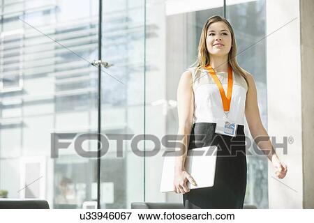 Smiling businesswoman holding laptop while standing in office View Large Photo Image Stock Photo - Smiling businesswoman holding laptop while standing in office. Fotosearch