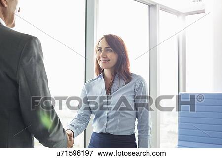 Stock Photo - Smiling businesswoman shaking hands with businessman in office. Fotosearch