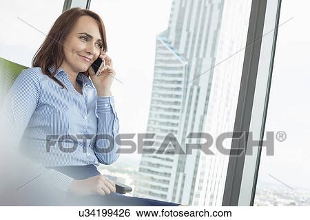 Stock Photograph - Smiling businesswoman talking on cell phone in office. Fotosearch