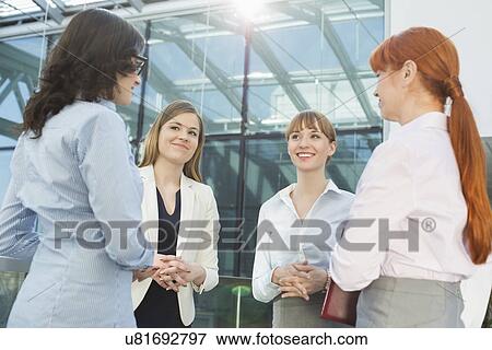 Stock Photo - Smiling businesswomen conversing in office. Fotosearch