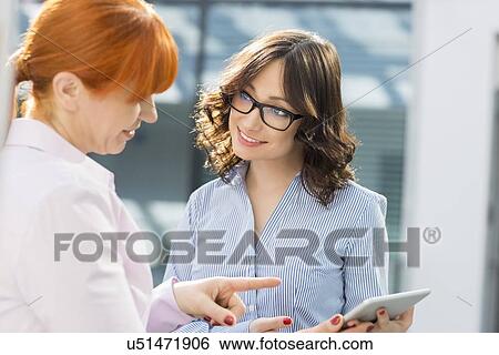 Smiling businesswomen discussing over tablet PC in office View Large Photo Image Stock Photograph - Smiling businesswomen discussing over tablet PC in office. Fotosearch