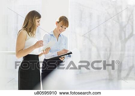 Smiling businesswomen with tablet PC and folder working by railing in office View Large Photo Image Stock Image - Smiling businesswomen with tablet PC and folder working by railing in office. Fotosearch