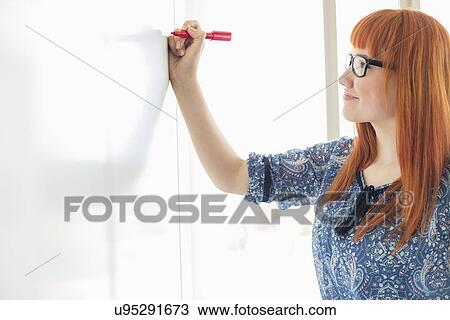 Stock Image - Smiling businesswomen writing on whiteboard in creative office. Fotosearch