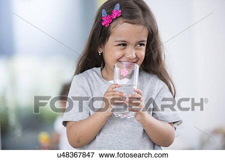 Smiling cute girl holding glass of water at home View Large Photo Image Stock Photo - Smiling cute girl holding glass of water at home. Fotosearch