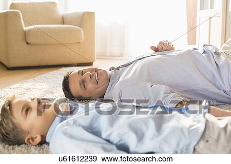 Stock Photo - Smiling father and son relaxing on floor at home. Fotosearch