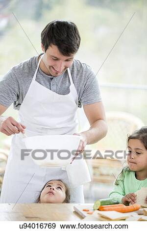 Stock Photo - Smiling father preparing sandwich with daughters at home. Fotosearch