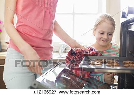 Smiling looking at mother removing cookie tray from oven at home View Large Photo Image Stock Photo - Smiling looking at mother removing cookie tray from oven at home. Fotosearch