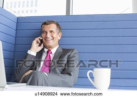 Picture - Smiling mature businessman talking on cell phone in office. Fotosearch