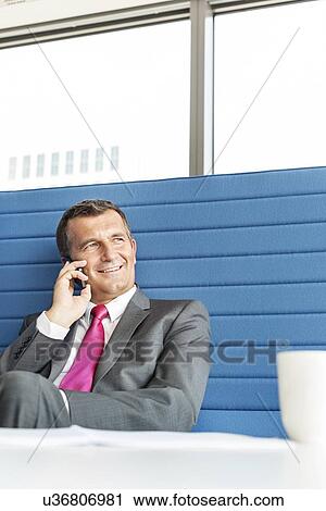 Stock Image - Smiling mature businessman talking on cell phone in office. Fotosearch