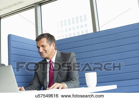 Smiling mature businessman using laptop at desk View Large Photo Image Stock Photograph - Smiling mature businessman using laptop at desk. Fotosearch