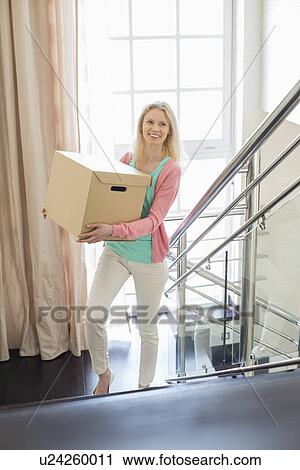 Smiling woman carrying cardboard box while moving up steps at new home View Large Photo Image Stock Image - Smiling woman carrying cardboard box while moving up steps at new home. Fotosearch