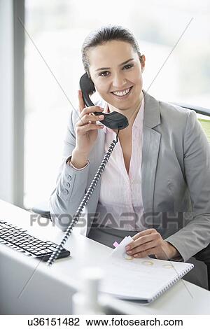 Stock Image - Smiling young businesswoman talking on telephone in office. Fotosearch