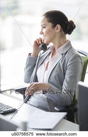 Smiling young businesswoman talking on landline phone in office View Large Photo Image Stock Photography - Smiling young businesswoman talking on landline phone in office. Fotosearch