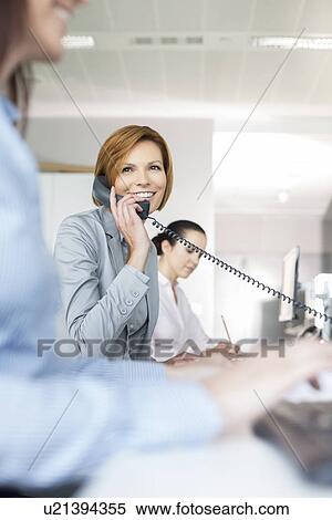 Smiling young businesswoman using landline phone in office View Large Photo Image Stock Photography - Smiling young businesswoman using landline phone in office. Fotosearch