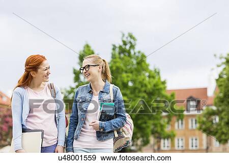 Stock Photo - Smiling young female college friends walking outdoors. Fotosearch