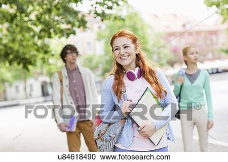 Stock Image - Smiling young female student with friends in background on street. Fotosearch