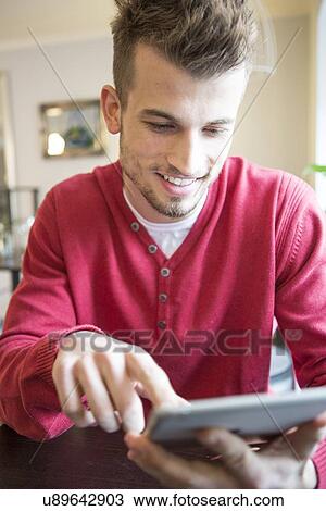 Stock Image - Smiling young man using tablet PC in cafe. Fotosearch