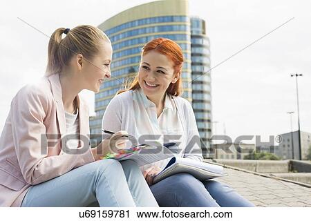 Stock Image - Smiling young university students studying against building. Fotosearch