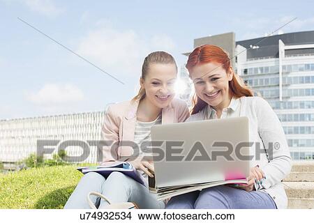 Picture - Smiling young university students using laptop with buildings in background. Fotosearch