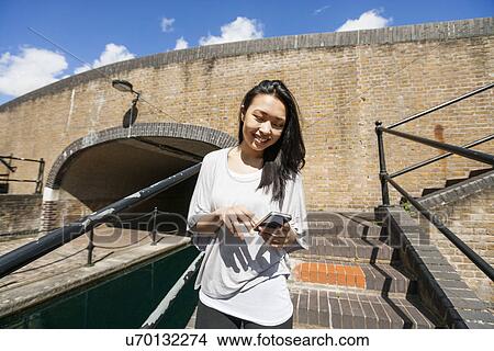 Picture - Smiling young woman using smart phone on stairs. Fotosearch