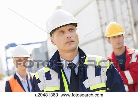 Stock Image - Team of confident workers in shipping yard. Fotosearch