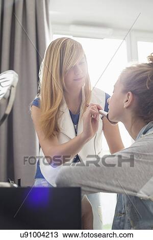 Teenage girl putting makeup on sister at home View Large Photo Image Stock Image - Teenage girl putting makeup on sister at home. Fotosearch