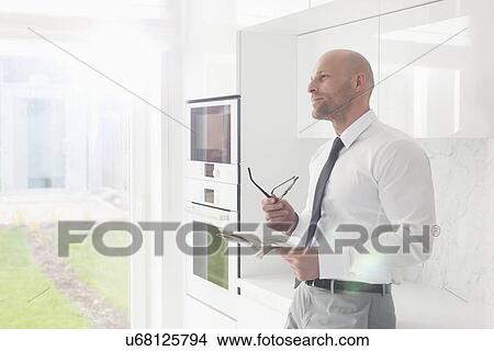 Thoughtful businessman holding newspaper at home View Large Photo Image Picture - Thoughtful businessman holding newspaper at home. Fotosearch