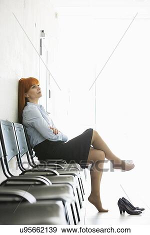 Thoughtful businesswoman sitting with legs crossed on chair in office View Large Photo Image Stock Photo - Thoughtful businesswoman sitting with legs crossed on chair in office. Fotosearch