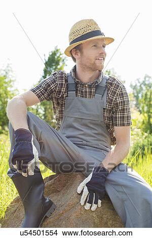 Picture - Thoughtful gardener looking away while sitting on rock. Fotosearch