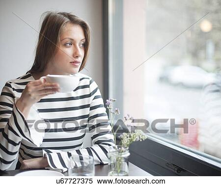Thoughtful young woman looking out from window while drinking coffee in cafe View Large Photo Image Stock Photography - Thoughtful young woman looking out from window while drinking coffee in cafe. Fotosearch