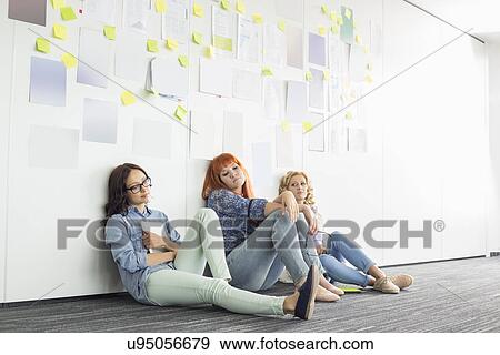 Stock Photo - Tired businesswomen sitting on floor in creative office. Fotosearch