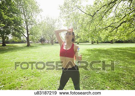 Stock Photo - Tired fit woman with water bottle listening to music in park. Fotosearch