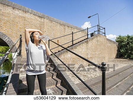 Tired young woman drinking water on stairs View Large Photo Image Stock Photo - Tired young woman drinking water on stairs. Fotosearch