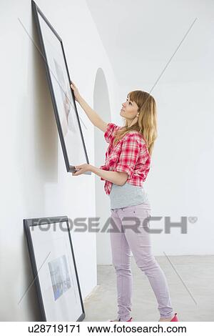 Woman hanging picture frame on wall in new house View Large Photo Image Stock Image - Woman hanging picture frame on wall in new house. Fotosearch