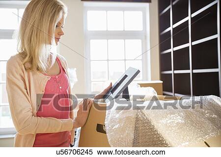 Stock Photography - Woman looking at photo frame while unpacking moving boxes at new house. Fotosearch