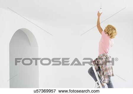 Stock Photo - Woman on ladder fitting light bulb in new house. Fotosearch