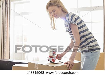 Stock Photo - Woman packing moving box at home. Fotosearch