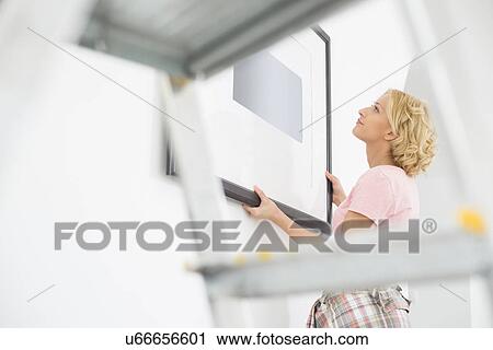 Woman positioning picture frame on wall View Large Photo Image Stock Image - Woman positioning picture frame on wall. Fotosearch