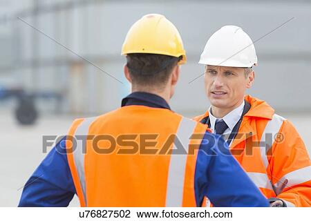Stock Image - Workers conversing in shipping yard. Fotosearch