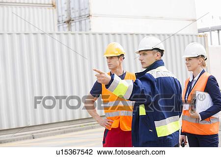 Stock Image - Workers discussing in shipping yard. Fotosearch