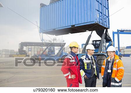 Stock Image - Workers discussing in shipping yard. Fotosearch