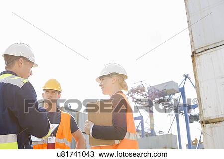 Stock Image - Workers discussing in shipping yard. Fotosearch