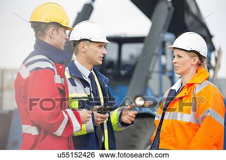 Stock Photograph - Workers discussing in shipping yard. Fotosearch